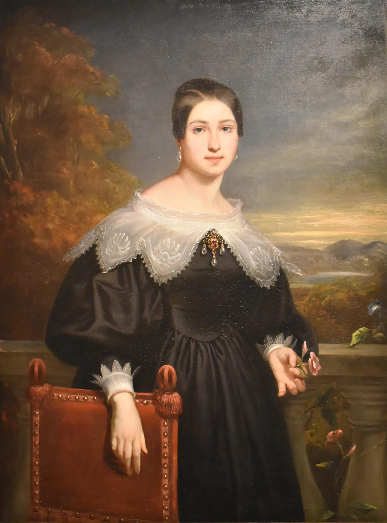 Self-Portrait Self-Portrait by Adélaïde-Élisa de Chénier. A three-quarter length portrait of a woman in a high-waisted dark dress with an intricate white lace pelerine, standing on a terrace overlooking a soft landscape.