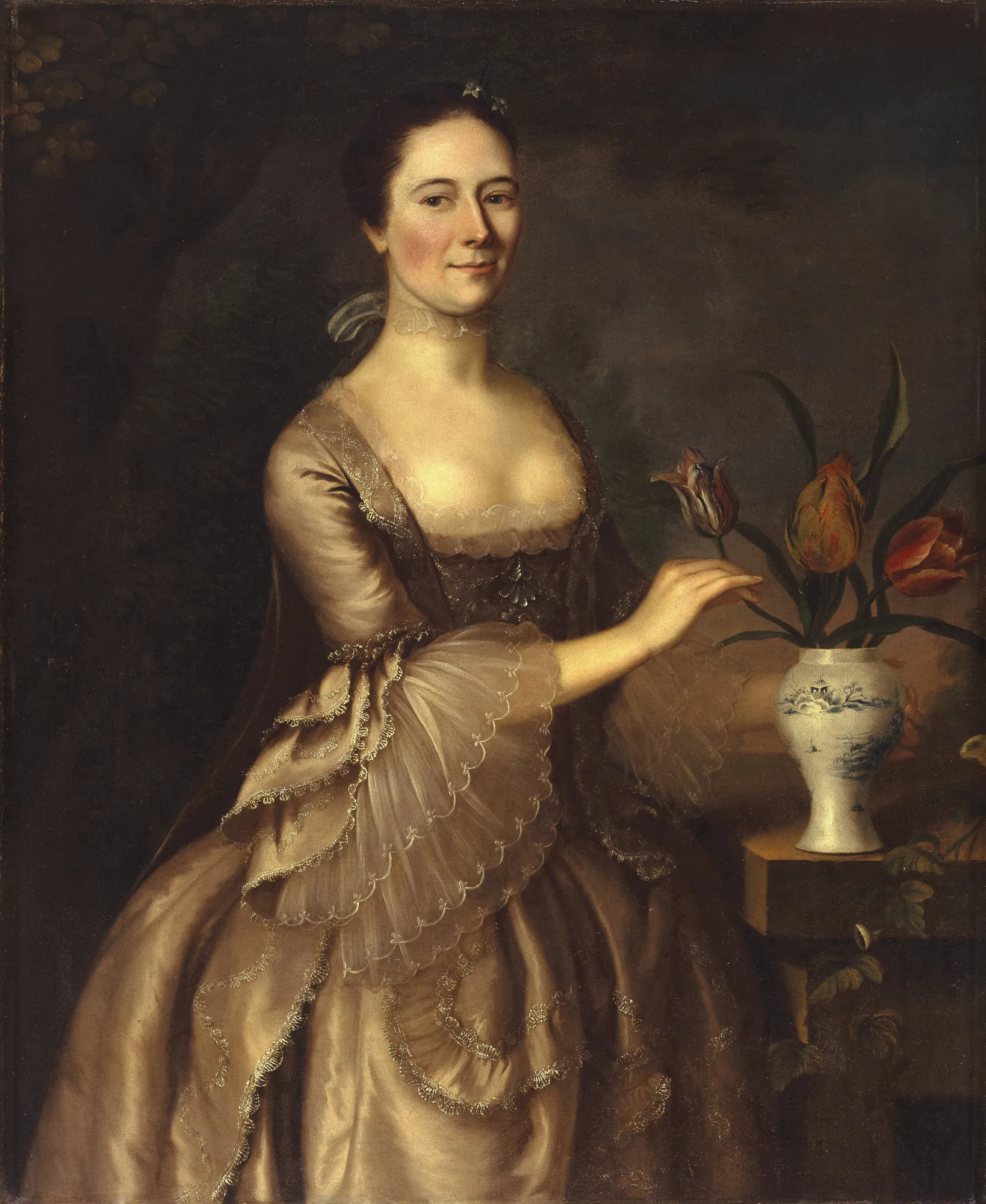 Portrait of a Woman Portrait of a Woman by Joseph Blackburn. An 18th-century portrait of a woman in a shimmering silk gown with elaborate lace ruffles, standing beside a blue and white vase filled with tulips.