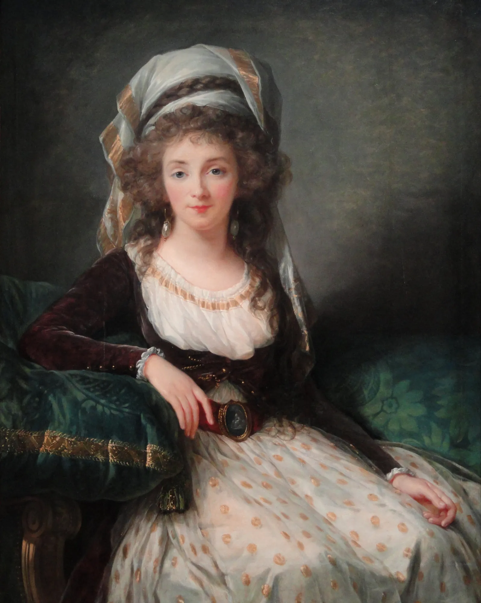 Madame d'Aguesseau de Fresnes Madame d'Aguesseau de Fresnes by Élisabeth Louise Vigée Le Brun. A woman with curled hair wearing an elaborate white and gold turban and a spotted gown rests against deep green cushions.
