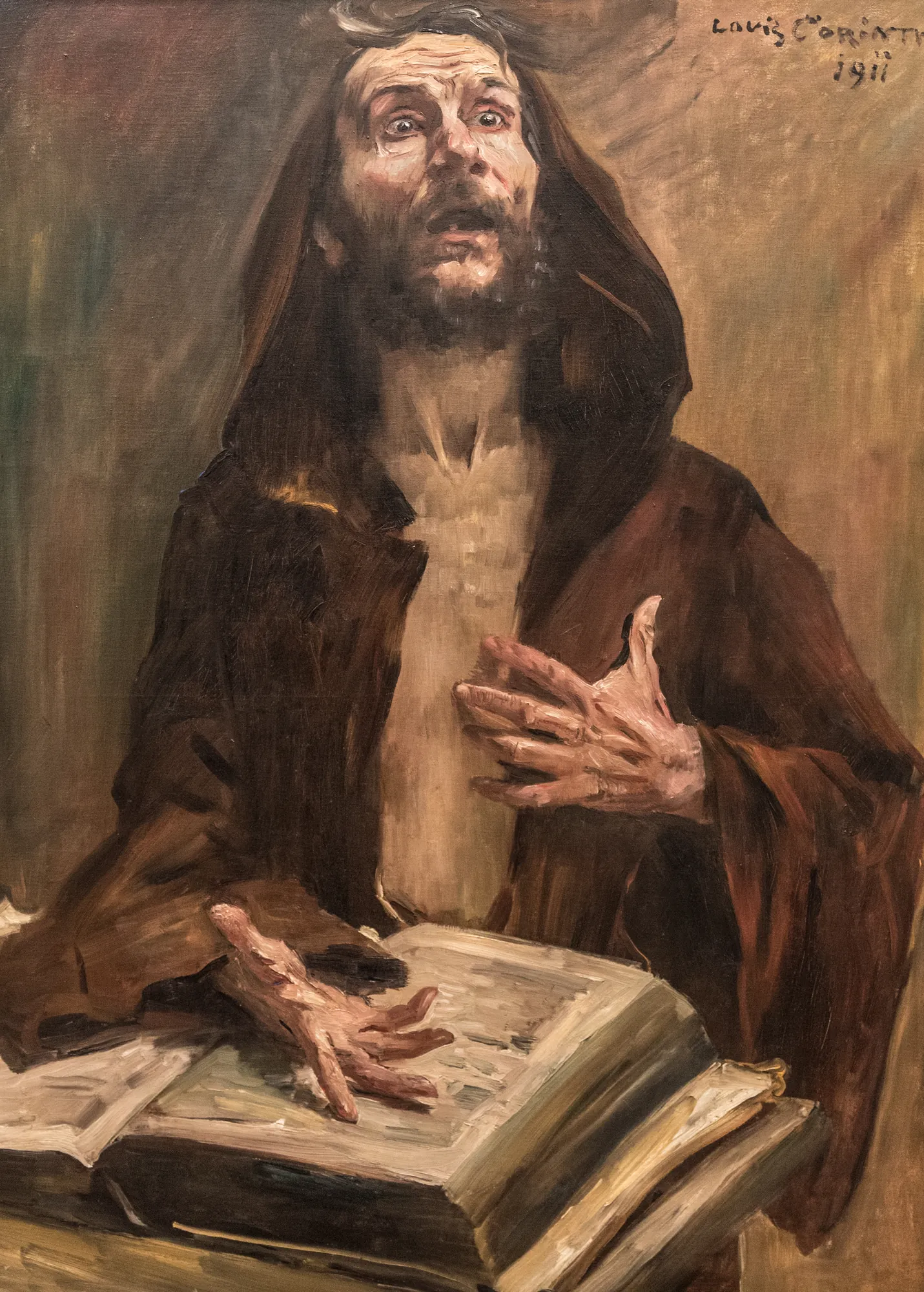 Der Fanatiker Der Fanatiker by Lovis Corinth. An intense, bearded man in a dark hooded robe looks upward with wide eyes and a gasping expression, his hands gesturing dramatically above a large open book.