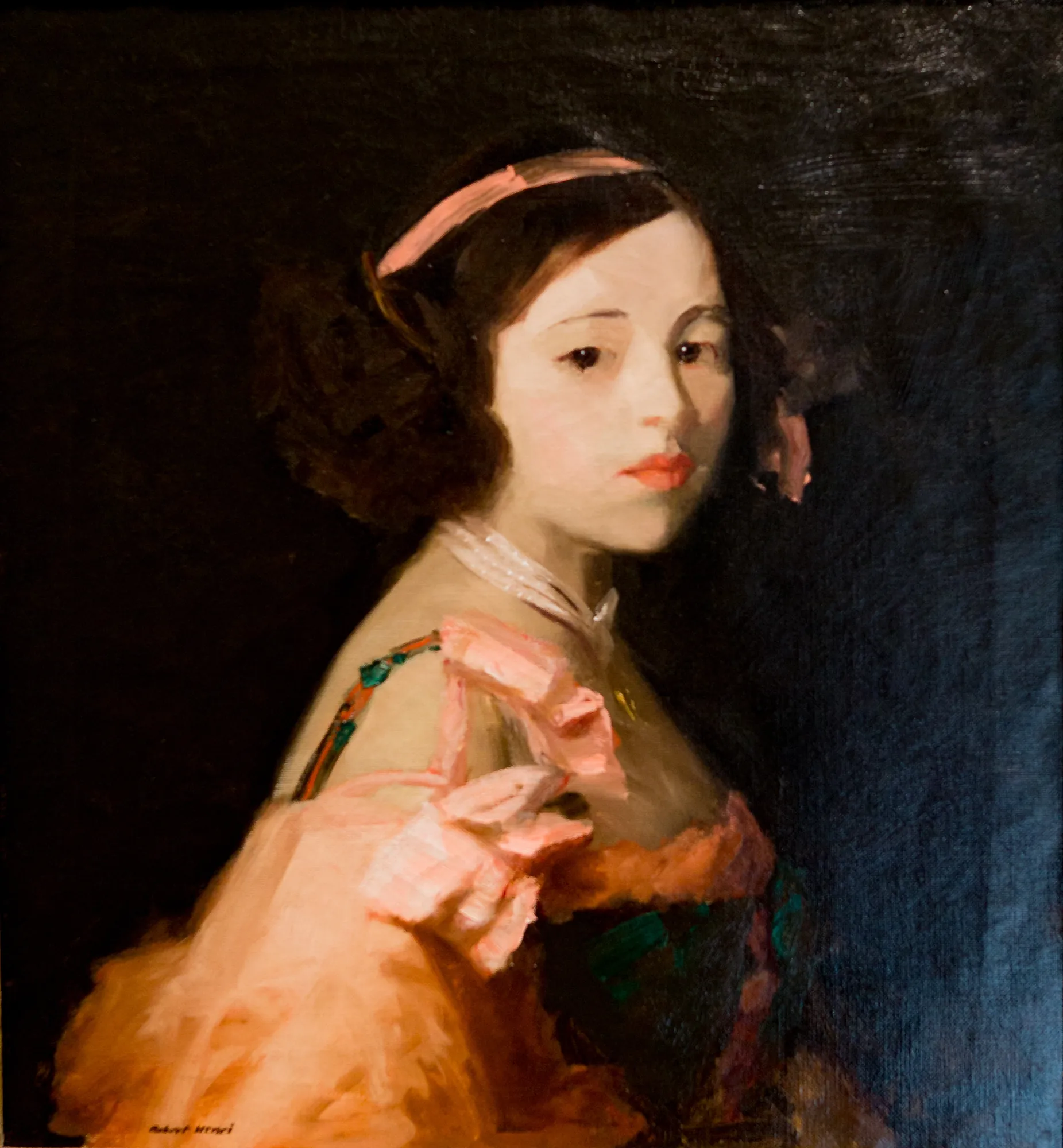 La Madrilenita La Madrilenita by Robert Henri. A portrait of a young girl with dark hair, a pink headband, and a ruffled pink gown set against a deep, dark background.