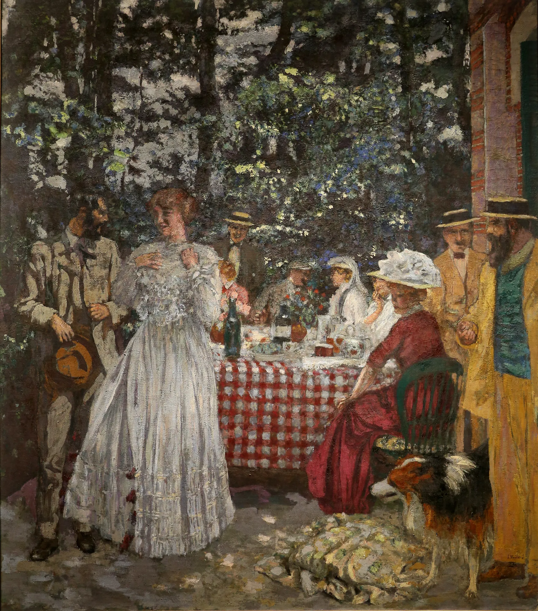 The Terrace at Vasouy, the Lunch The Terrace at Vasouy, the Lunch by Édouard Vuillard. A social gathering of elegantly dressed figures dining at a red checkered table on a sun-dappled terrace beneath dense trees.