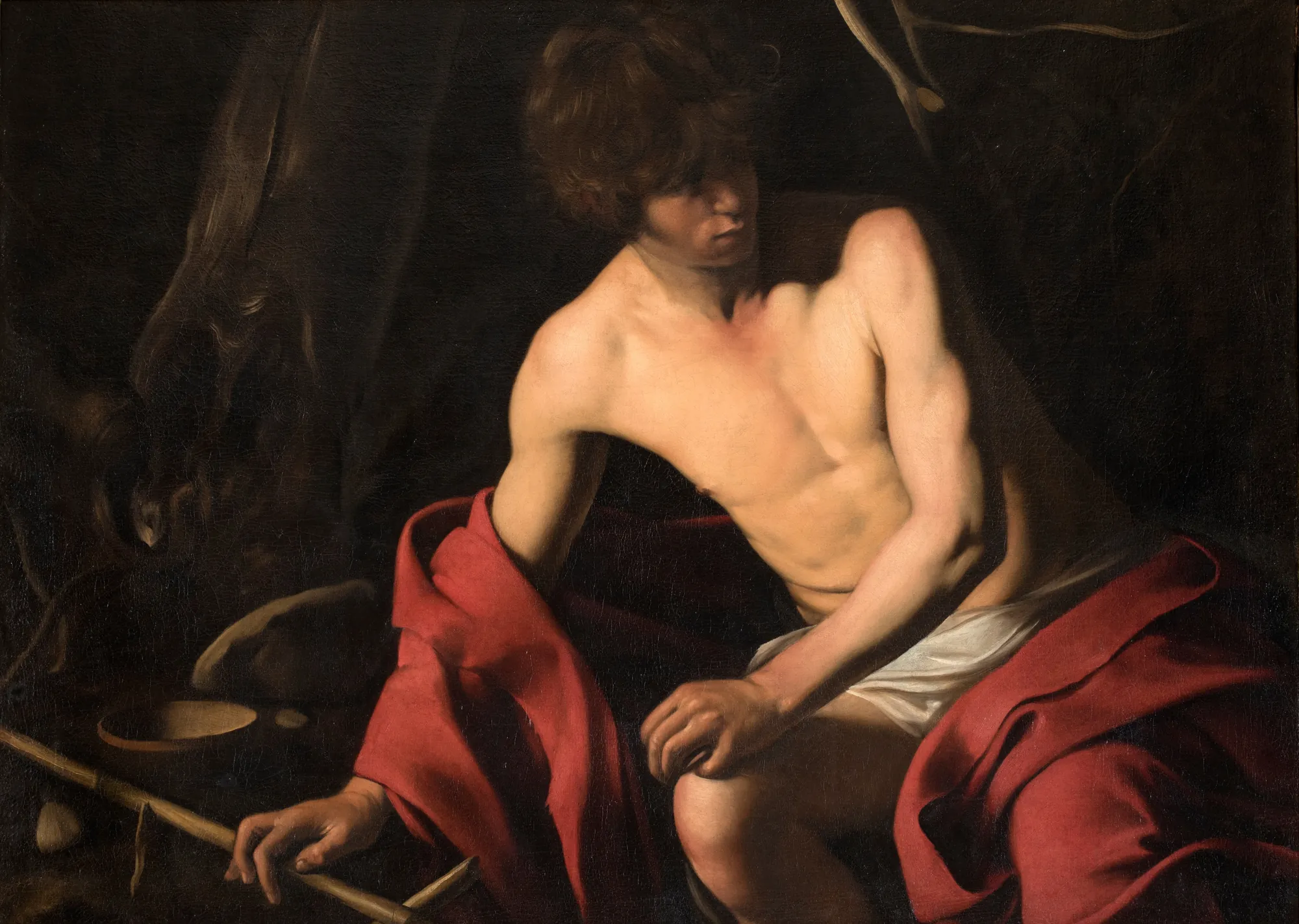 Saint John the Baptist Saint John the Baptist by Caravaggio. A bare-chested young man with curly hair sits in a dark, shaded setting, draped in a vibrant red cloak and white cloth.
