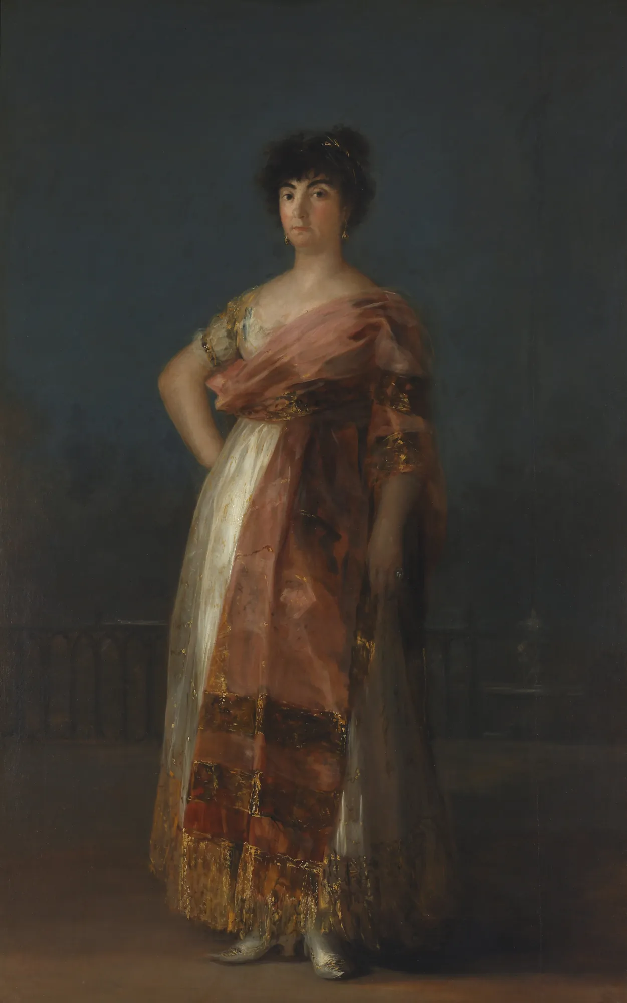 La Tirana La Tirana by Francisco Goya. A full-length portrait of a woman standing in a dark, atmospheric setting, wearing a white gown and a shimmering pinkish-red shawl.
