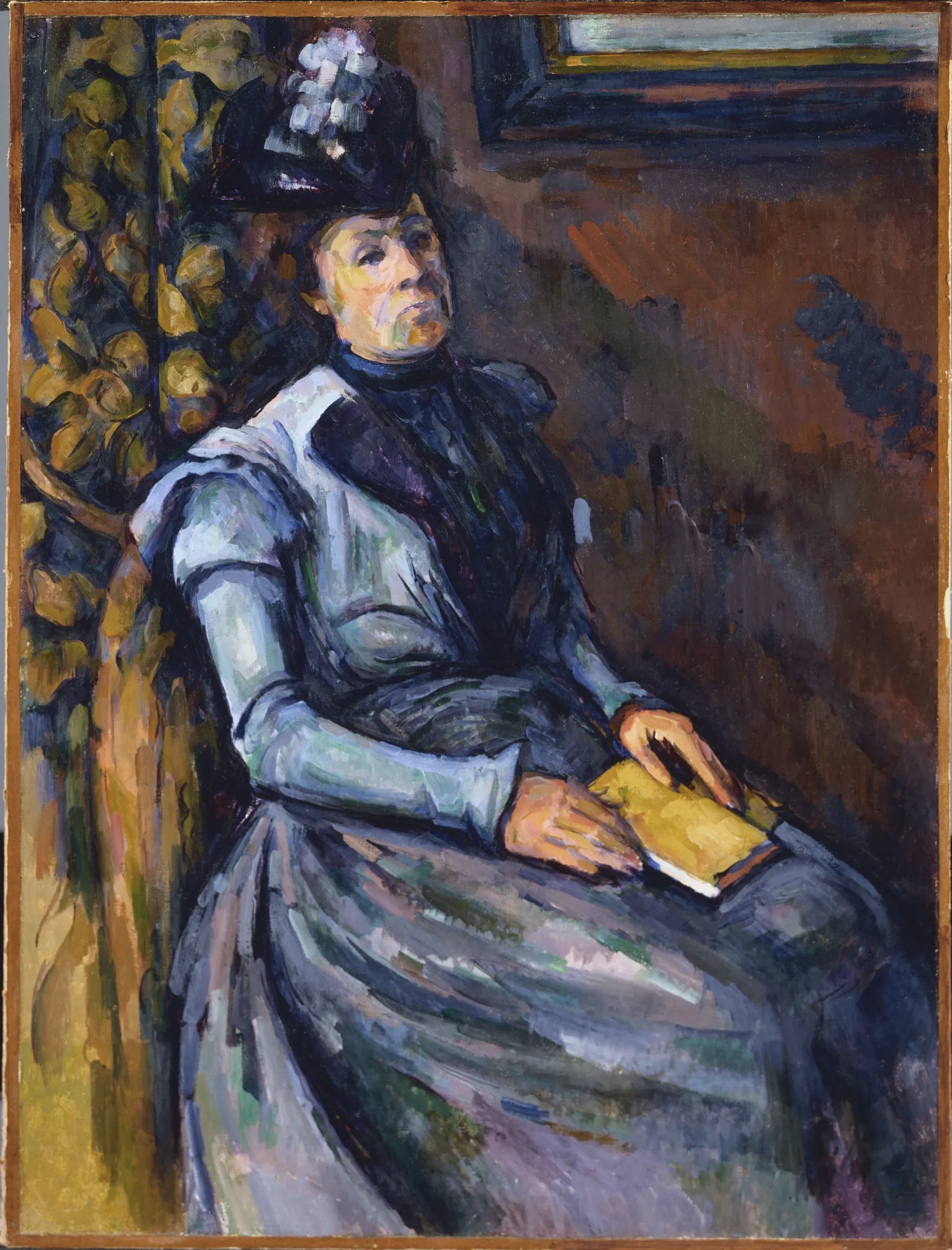 Seated Woman in Blue Seated Woman in Blue by Paul Cézanne. A portrait of a woman wearing a blue dress and a dark hat, seated with a book in her lap against a textured brown and green background.