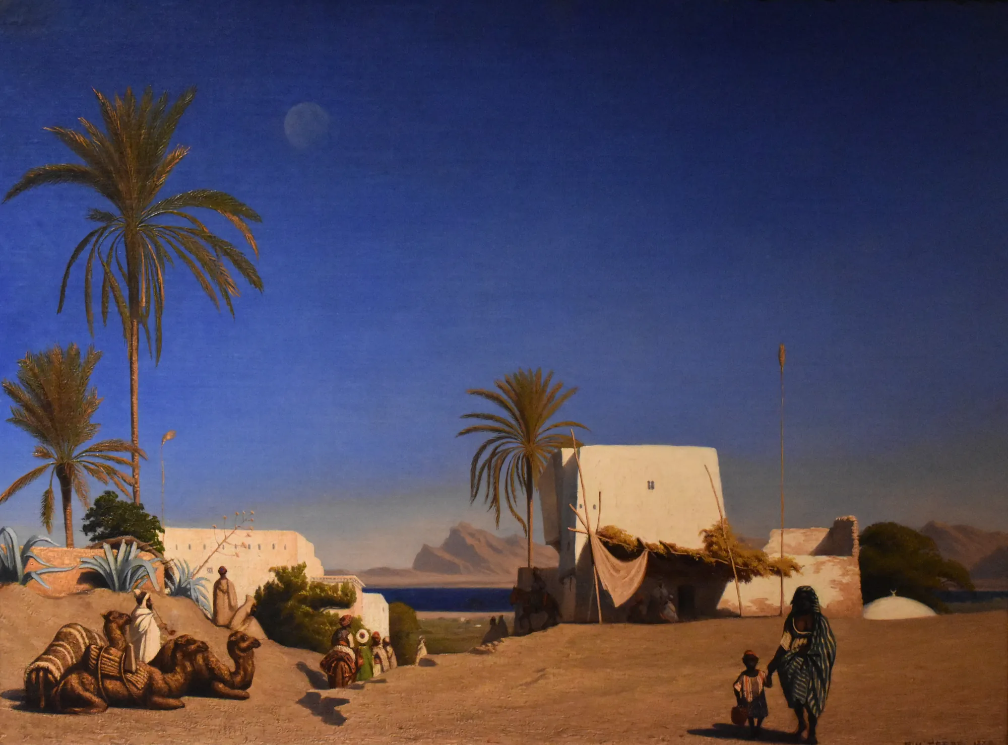 Algerian Landscape Algerian Landscape by Théodore Frère. A tranquil Algerian scene at twilight with palm trees, resting camels, and figures in traditional dress near white-walled buildings under a deep blue sky.